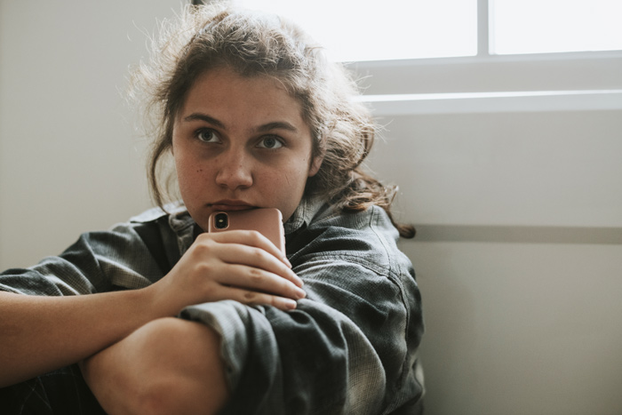 teenage girl holding cell phone and looking sad - substance use among young adults