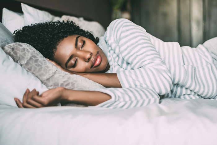 beautiful Black woman laying in bed with her eyes closed - sleep issues